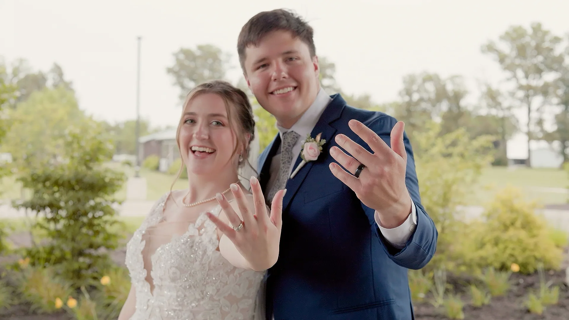 Bride and groom smiling and holding up their hands to show their wedding rings